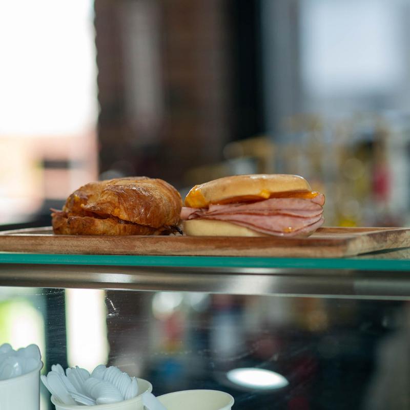 A close-up of a rustic food spread featuring a small bowl filled with mixed green and black olives on a wooden board, with a bowl of yogurt or dip and a salad in the background.