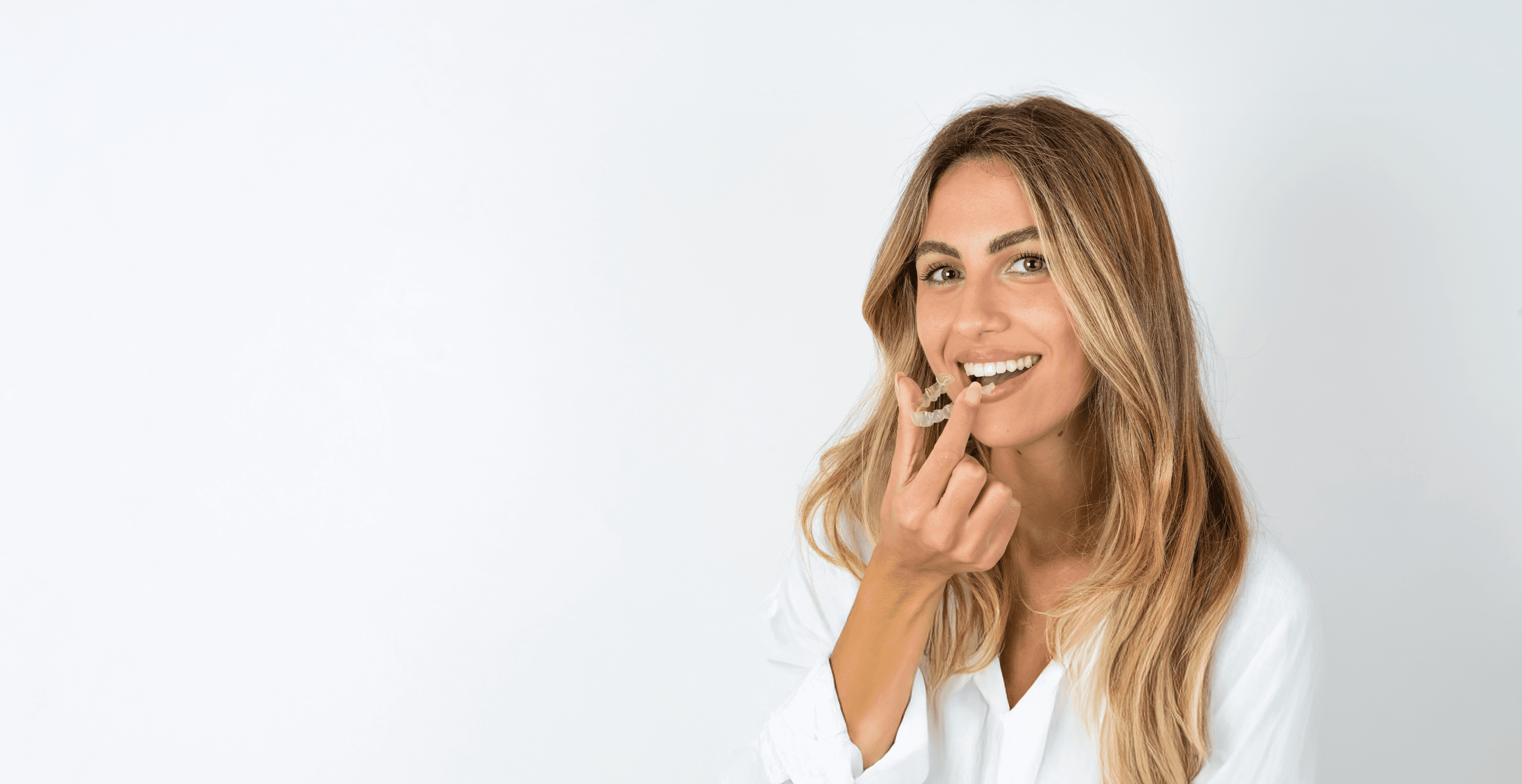 A woman smiles and holds invisalign clear aligners with a case, showcasing a certified invisalign provider at Bella Medical Centre