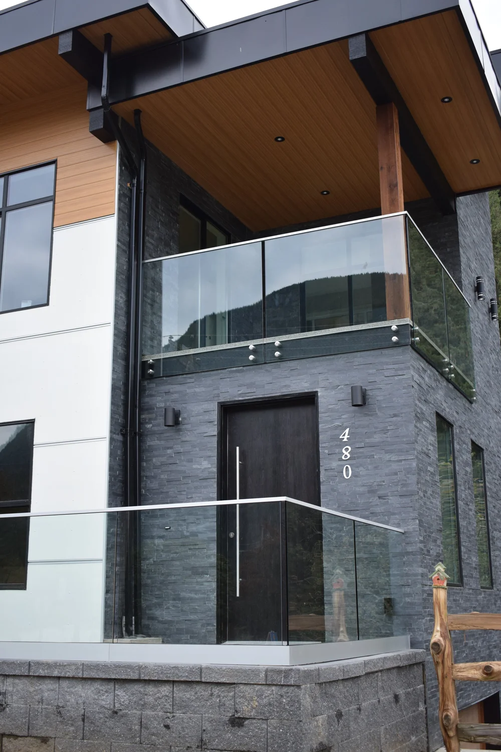House balcony glass design featuring steel-framed glass railing on a modern exterior with stone façade.