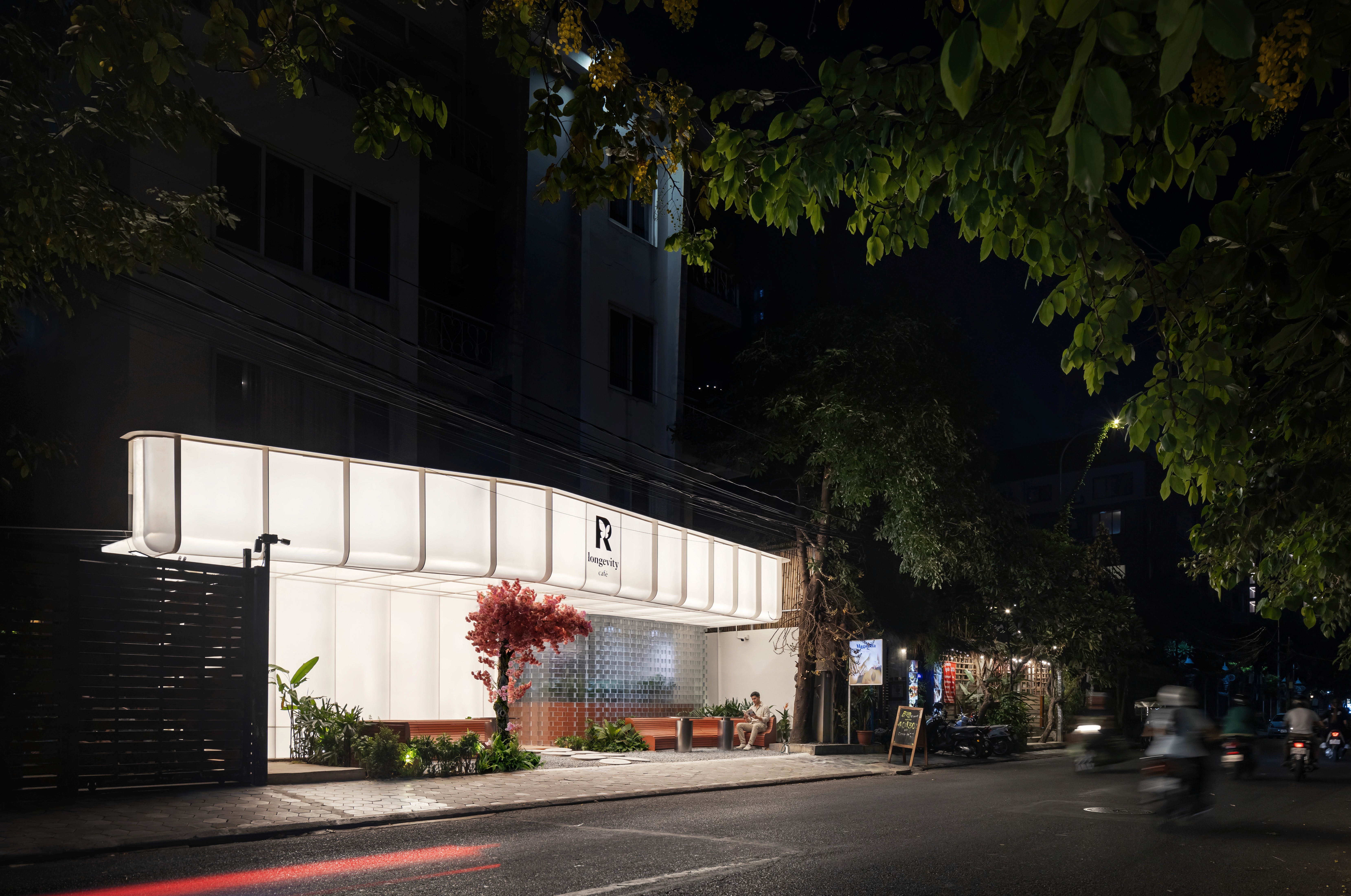 Full street view at night showing illuminated canopy, terrace seating, and glass-block feature composition, reinforcing brand presence