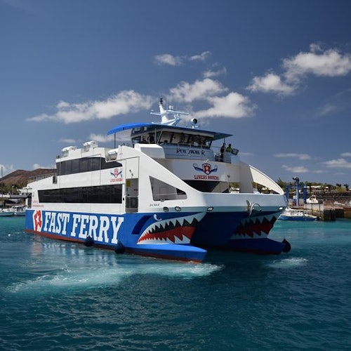 Large ferry boat labeled "FAST FERRY" on the side, sailing in clear blue water on a sunny day with a few clouds in the sky.