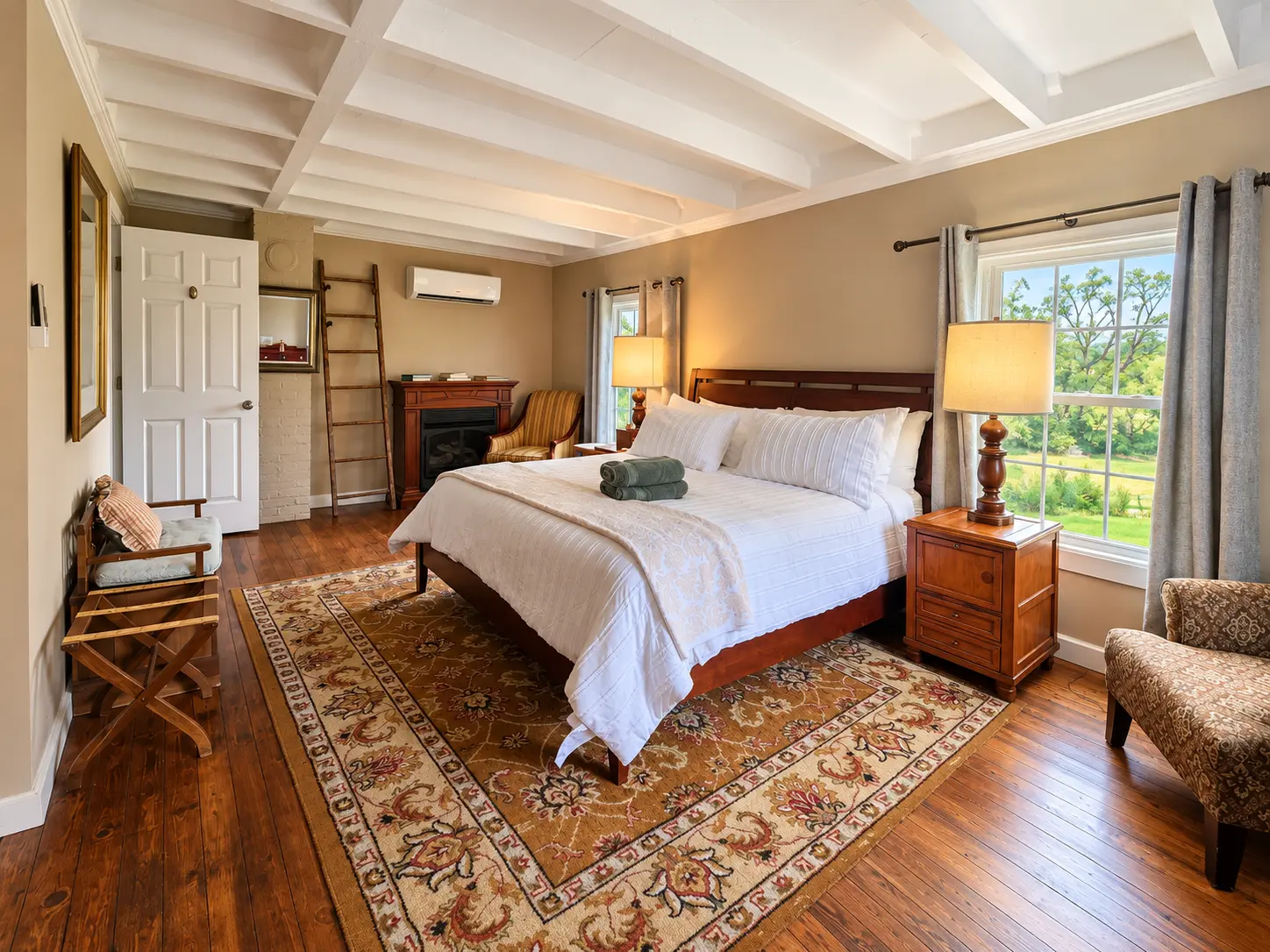 A cozy bedroom with a large bed, lit fireplace, and exposed ceiling beams.