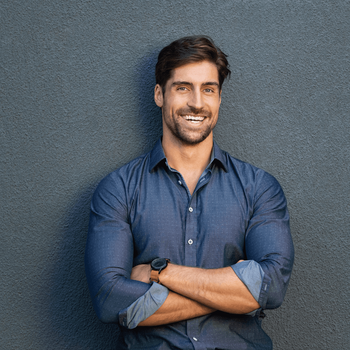 Smiling young man with short hair poses against a dark background, wearing a green button-up shirt.