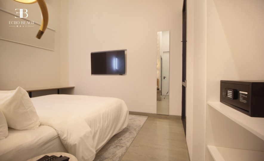 Bedroom of the Mezzanine apartment suite at Echo Beach, Canggu, Bali, with a wall-mounted TV and an in-room safe on shelving.