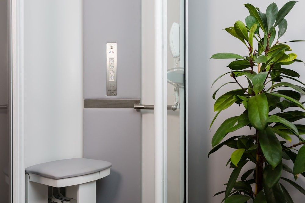 alt text for this image11:57Claude responded: Interior of an Elevate AVA Rise home lift cabin showing fold-down upholstered seat, stainless steel control panel with floor selection buttons, handrail, and g…Interior of an Elevate AVA Rise home lift cabin showing fold-down upholstered seat, stainless steel control panel with floor selection buttons, handrail, and glass door panel — white cabin finish with indoor plant visible alongside