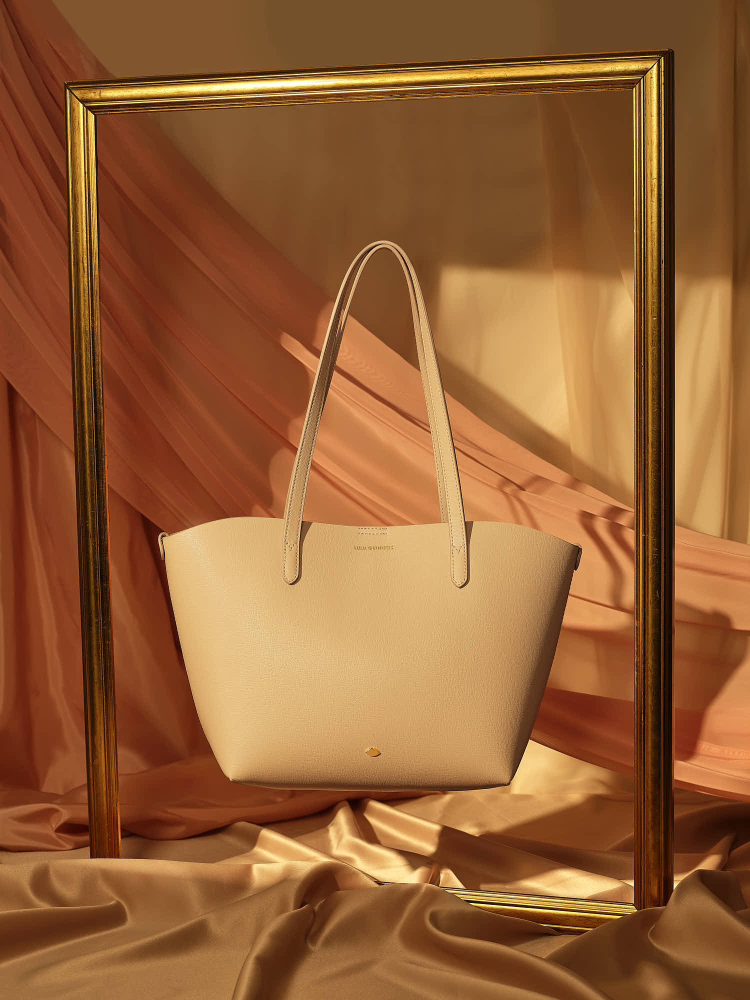 Elegant beige tote bag with gold accents, framed in stylish decor.