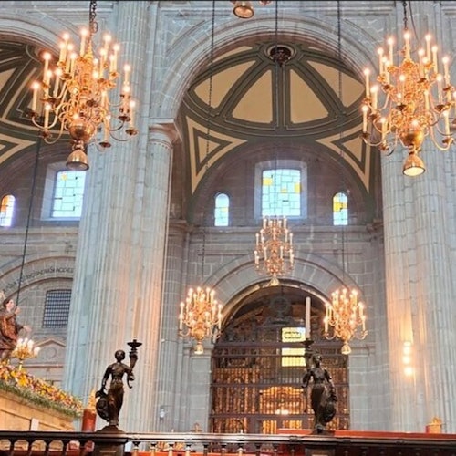 Loob ng isang malaking katedral na may mataas na arko, mga chandeliers, mga bintana ng makukulay na salamin, at mga magagarang rebulto.