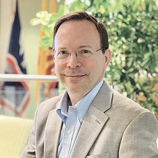 Ein Mann mit braunen Haaren und Brille im Anzug