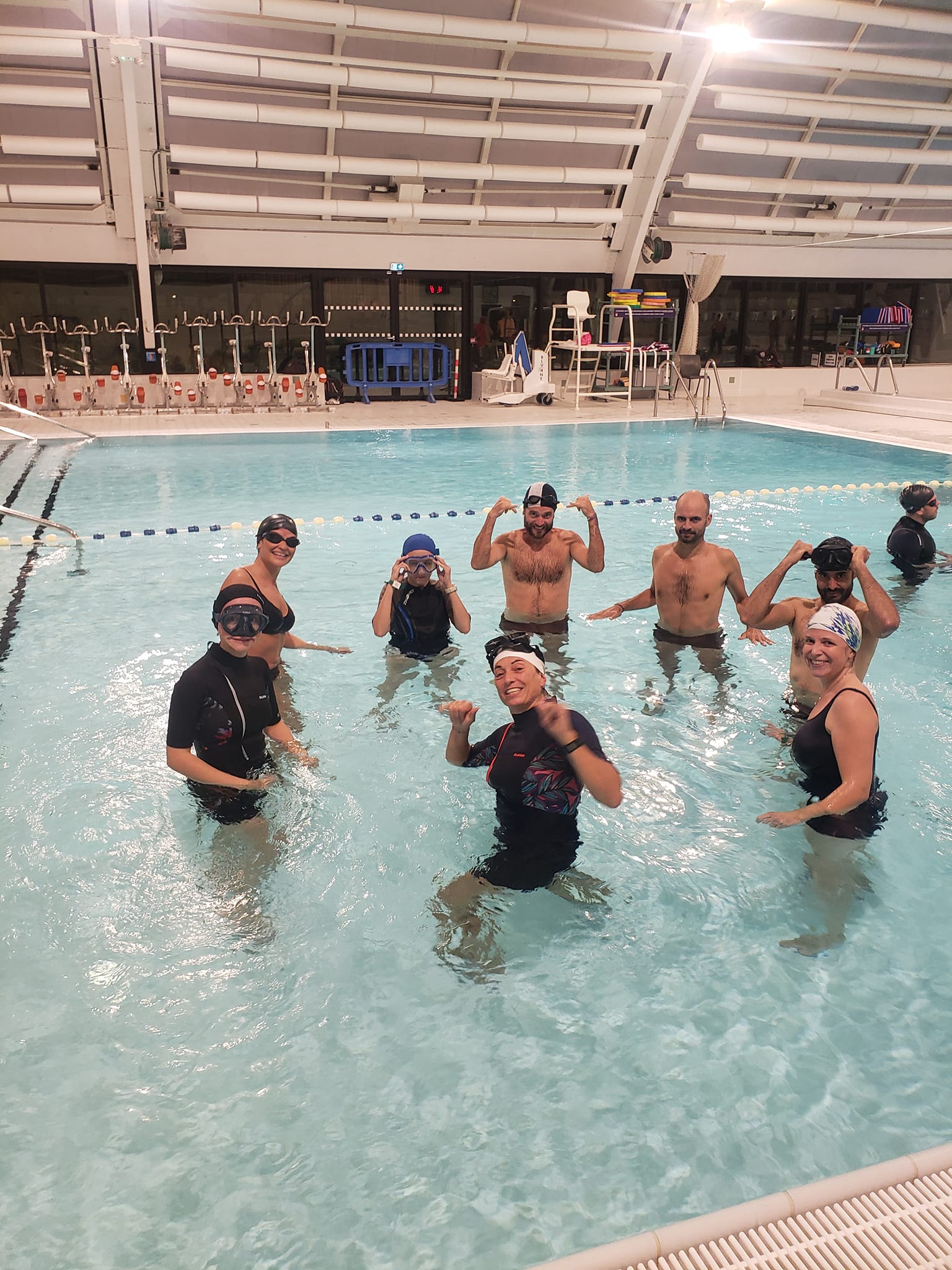 A young person with curly hair smiles at the camera while sitting in front of a laptop against a dark background.