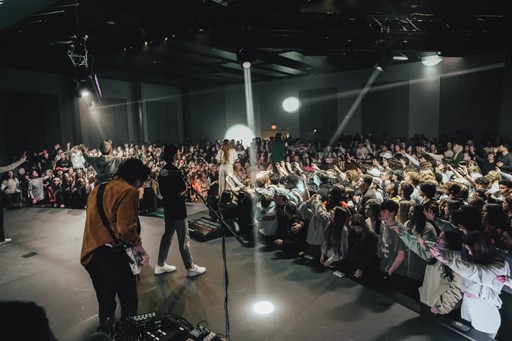 A group of four people standing outside a building, engaging in conversation, with cars parked nearby.