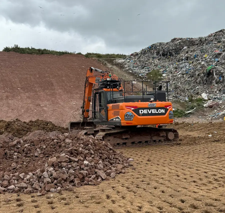 Excavator managing bulk construction waste and material stockpiles at a UK site clearance and waste handling operation.