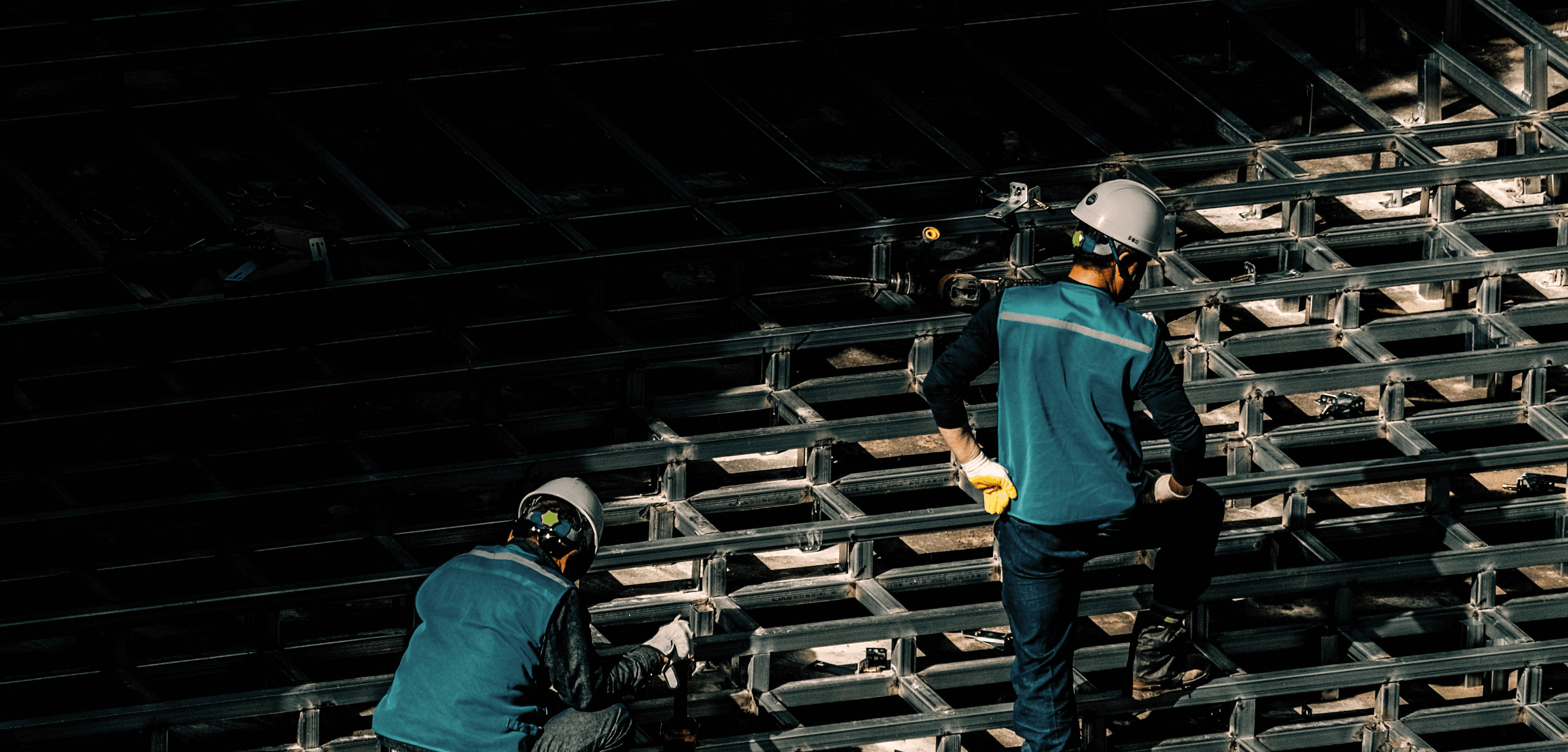 Two people in teal clothing are seen cleaning or inspecting empty seats in a dark auditorium.