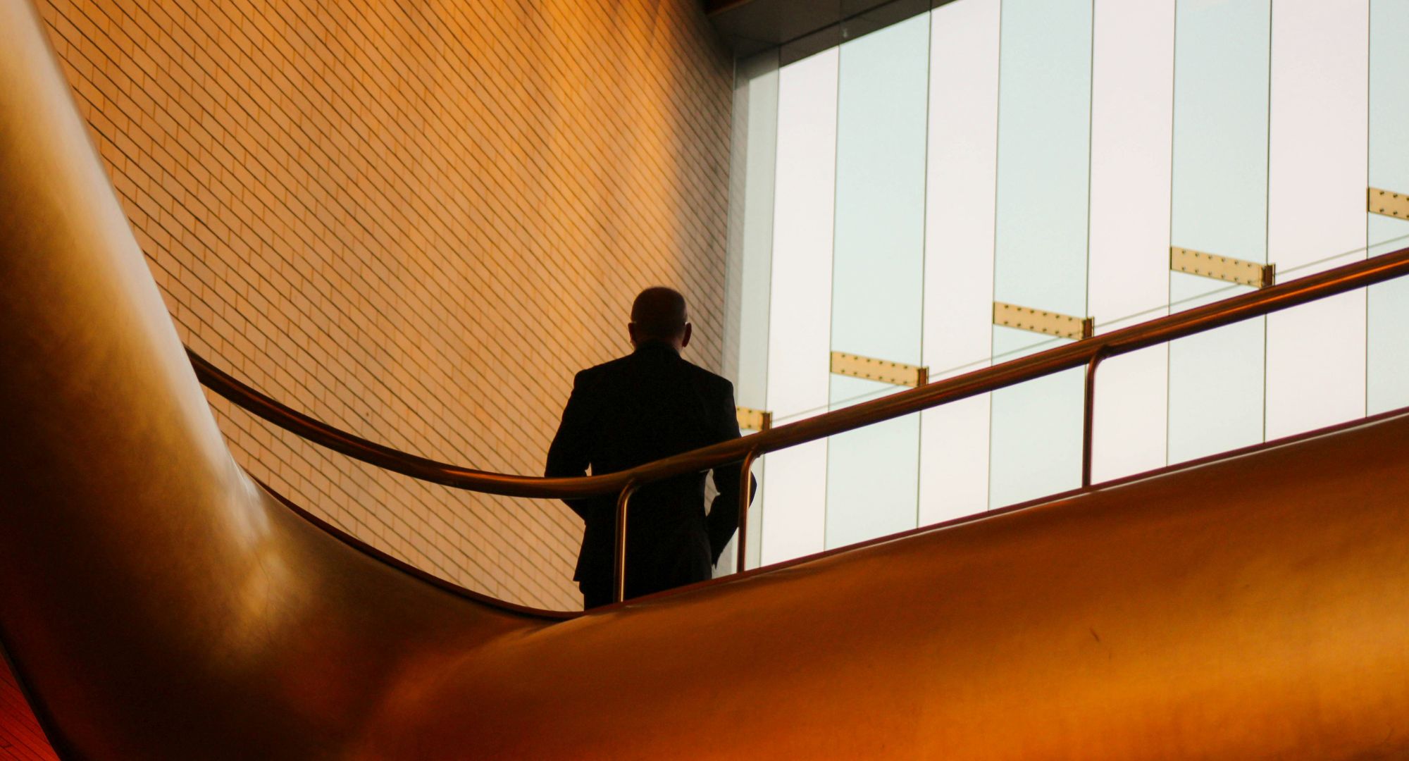 silhueta de um homem vestido de terno ao fundo de um lugar visualmente empresarial com cor laranja indireta e predominante