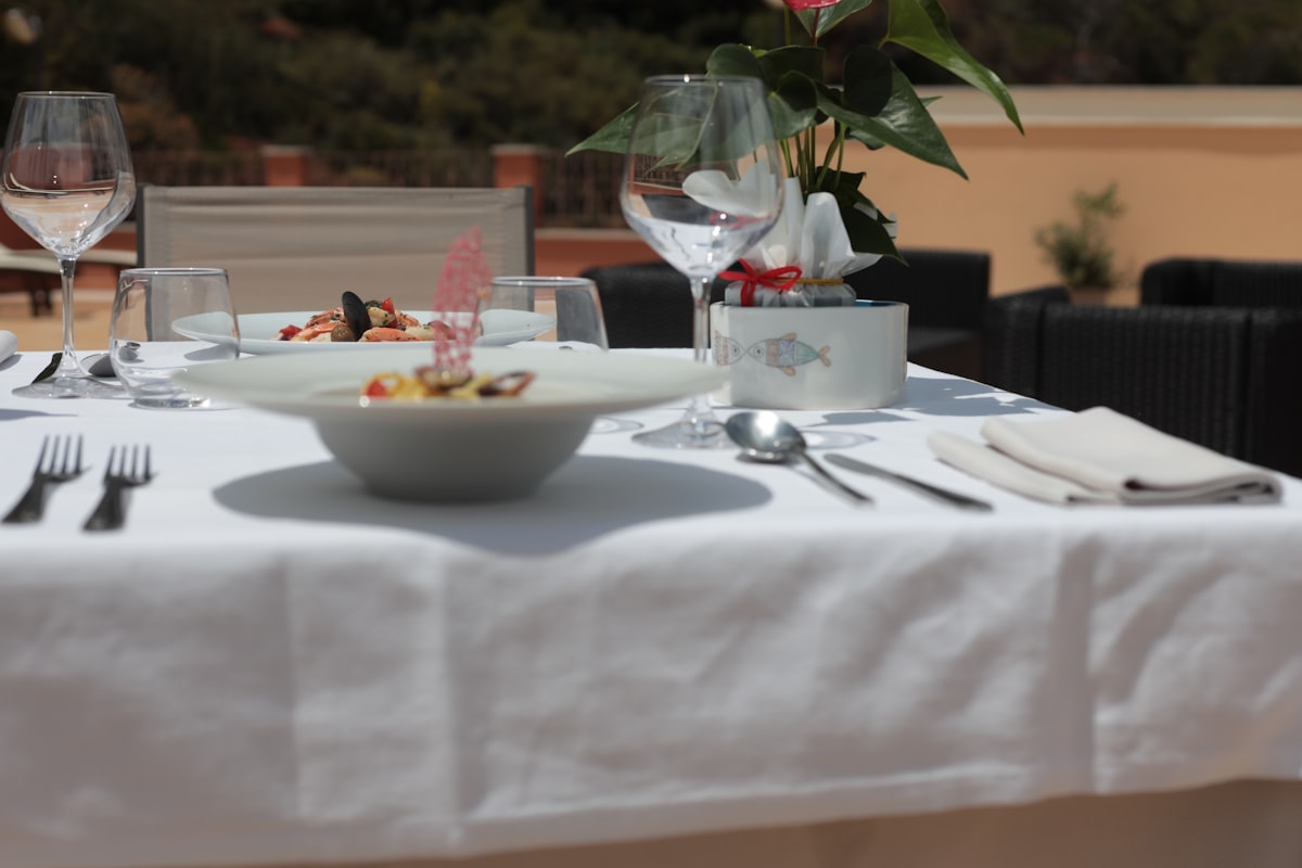 Outdoor Italian table setting with pasta, wine glasses, and bread at a sun-lit trattoria