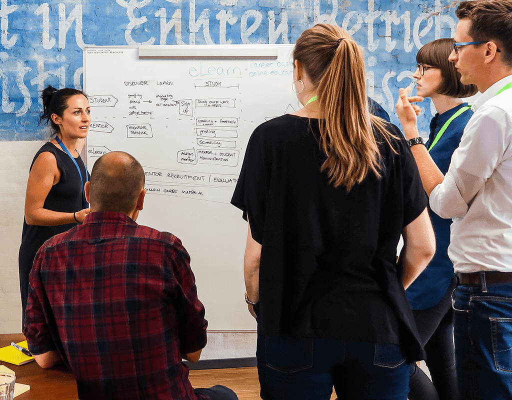 Remote workshop screenshot in Miro showing a Sailboat exercise with sticky notes and team video feeds