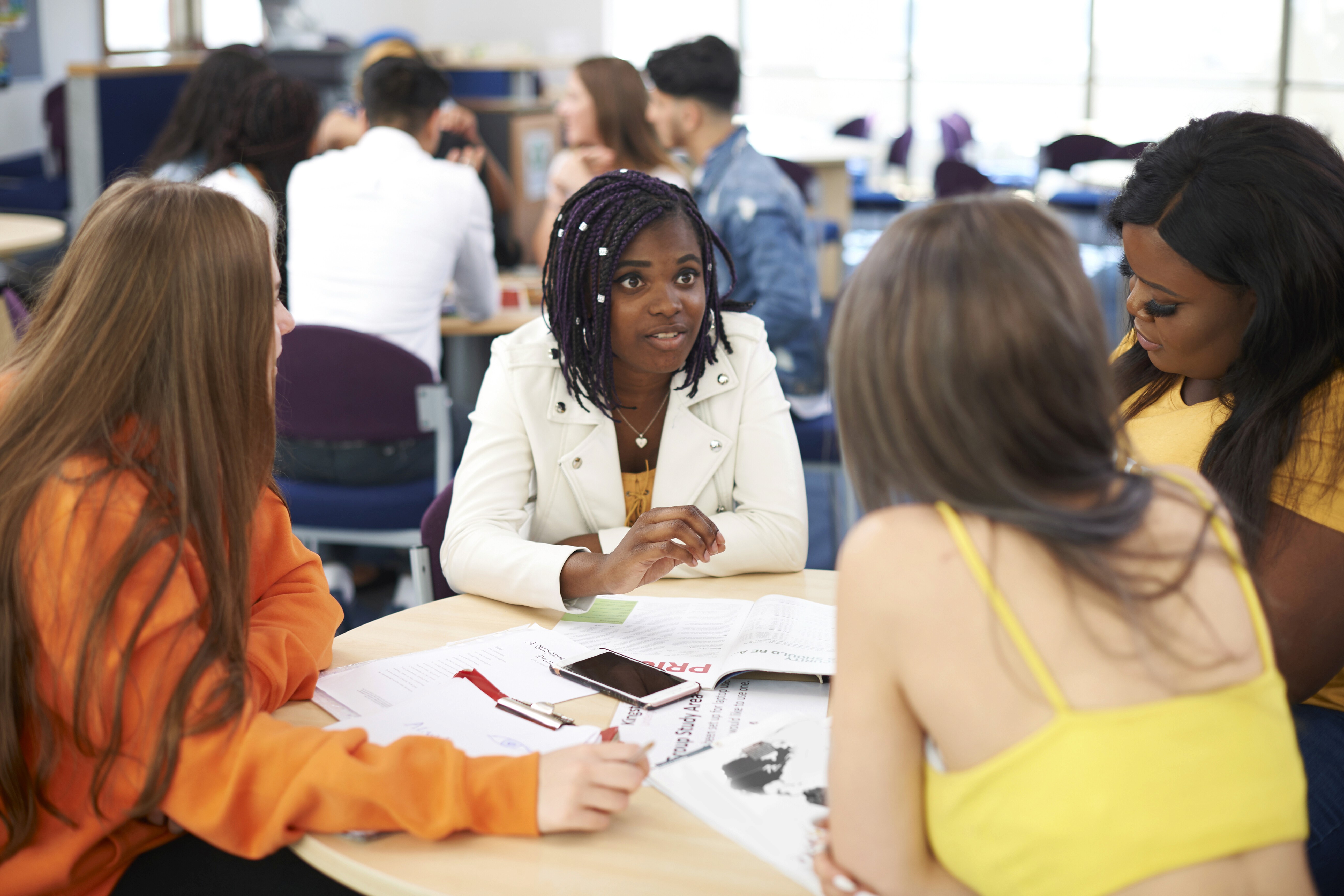 Group of girls seated around a table, actively engaging in a debate about an activity