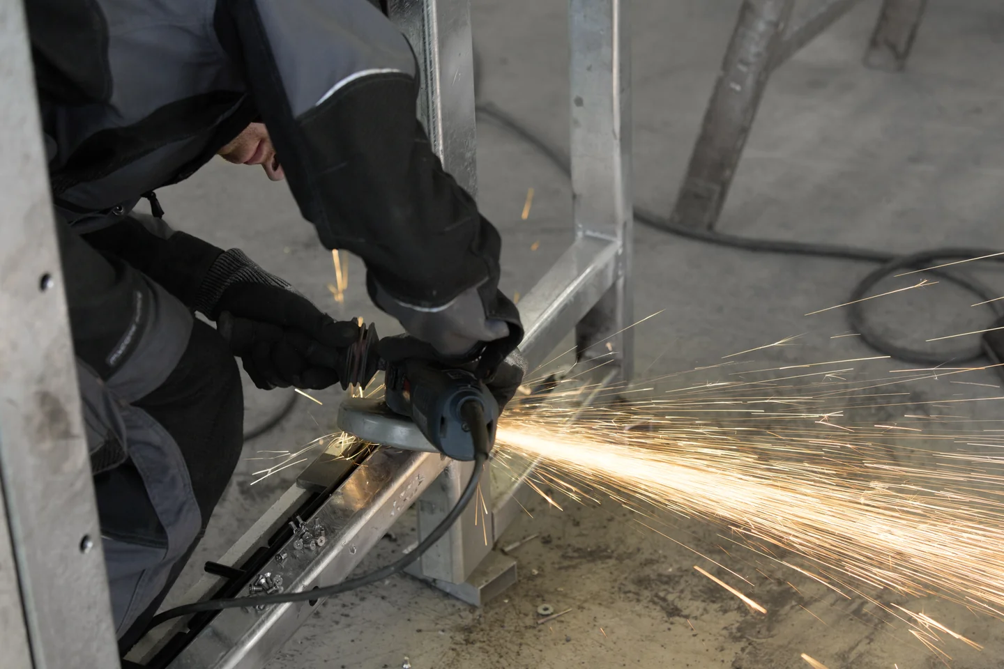 Ein Mitarbeiter bearbeitet einen Metallrahmen mit einem Winkelschleifer.