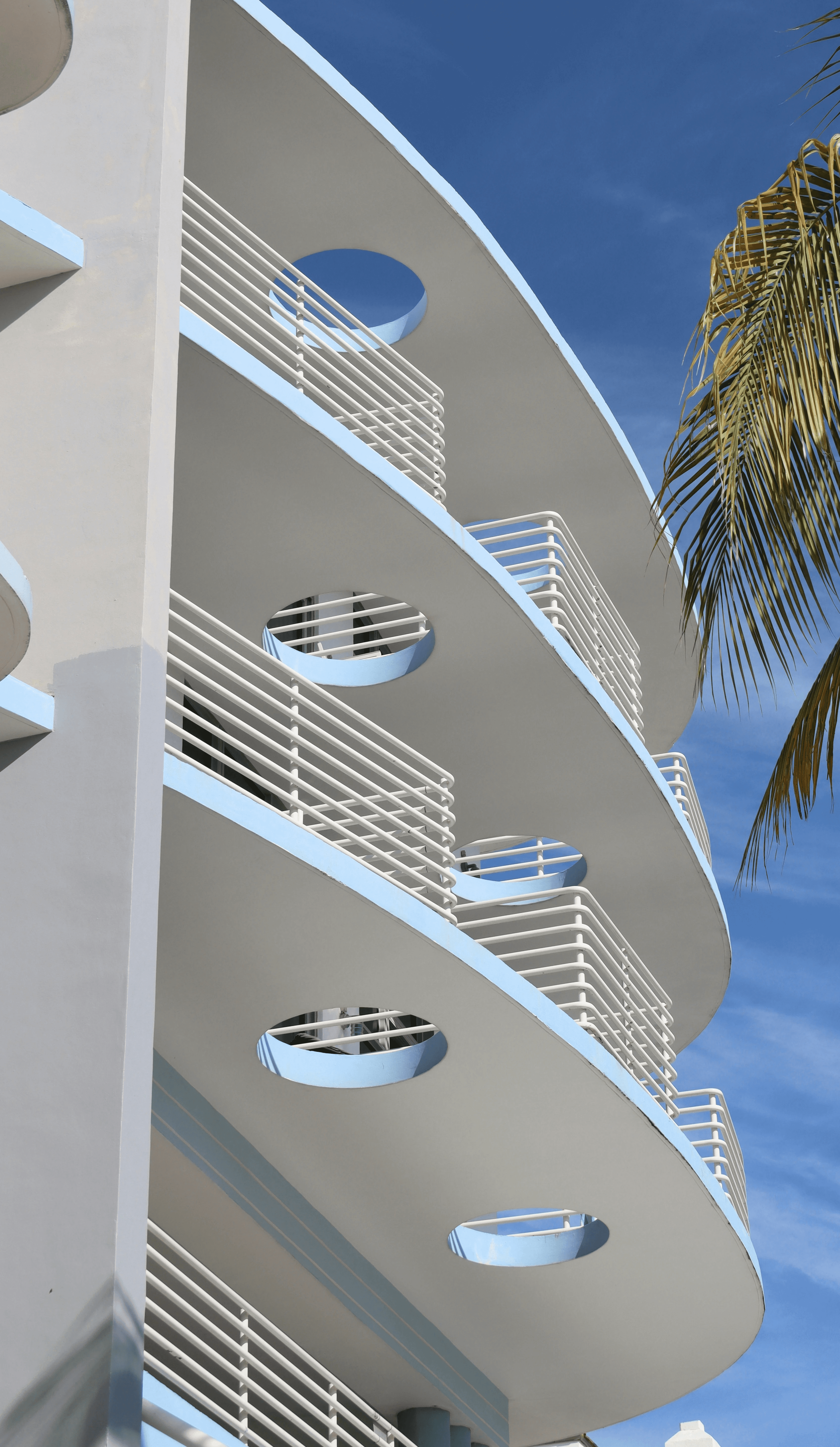 a tall white building with balconies next to a palm tree
