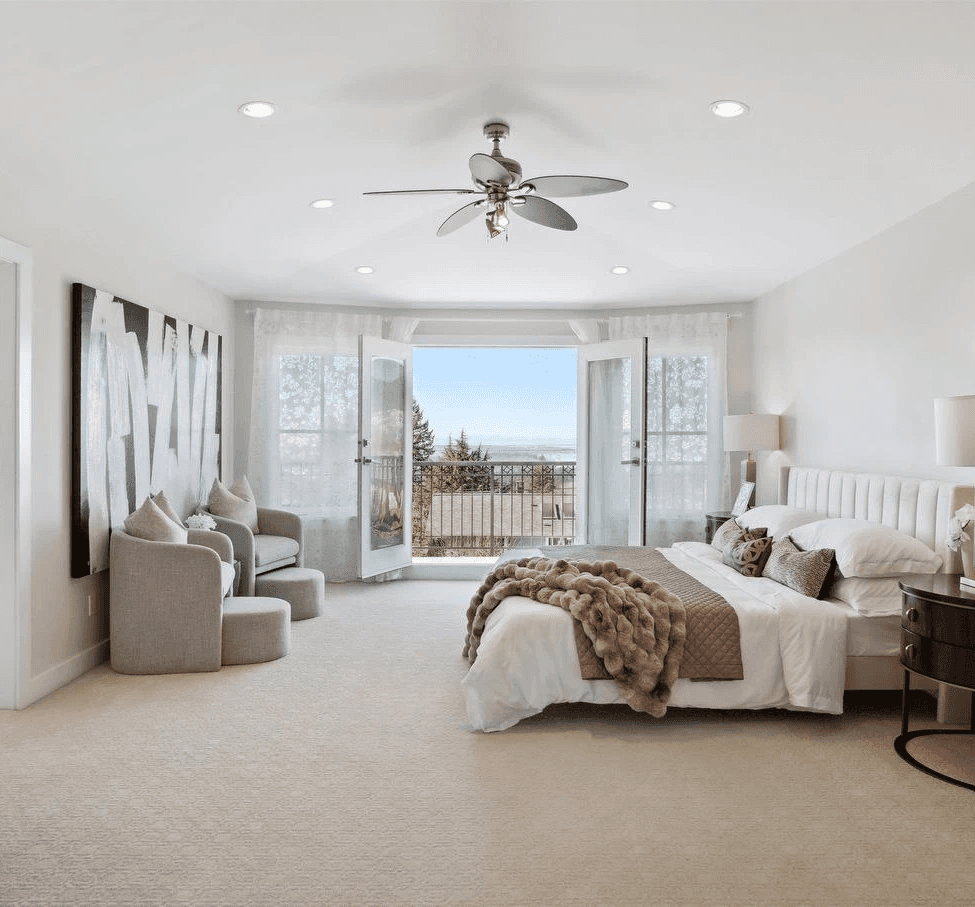 Bright, spacious bedroom with panoramic windows, a ceiling fan, and modern furnishings overlooking a scenic view.