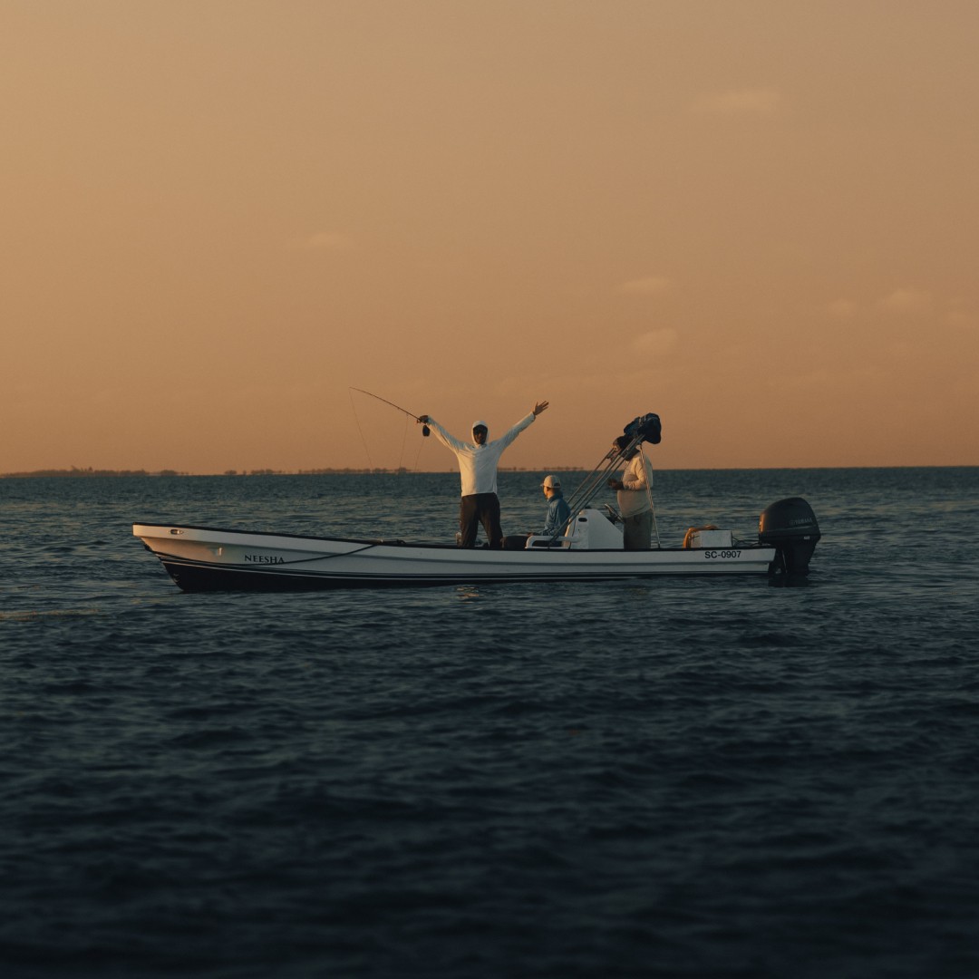 Two anglers and guide on flats skiff at dawn near Placencia, Belize