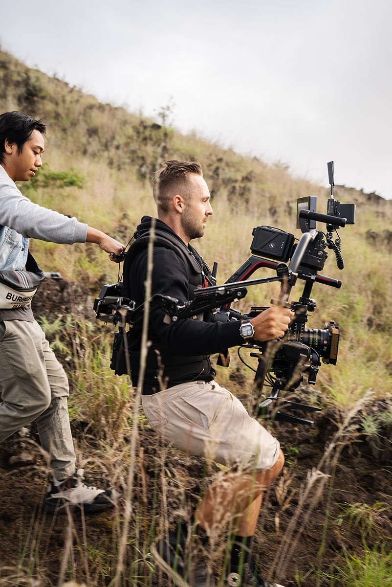 Behind-the-scenes of a creative production team filming in a forest, showing camera crew and equipment in action.