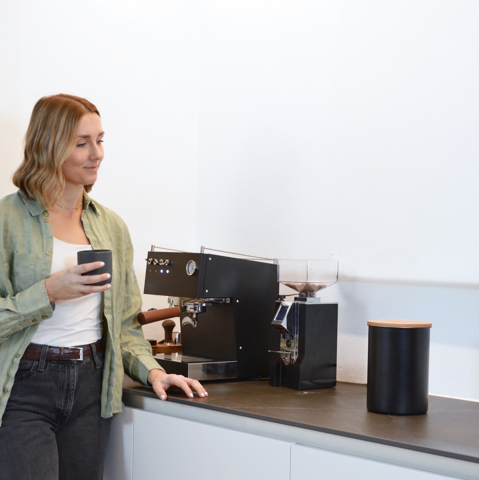 Close-up portrait of a person wearing a gray insulated hooded jacket with the hood up, showing their face framed by the hood against a light background.
