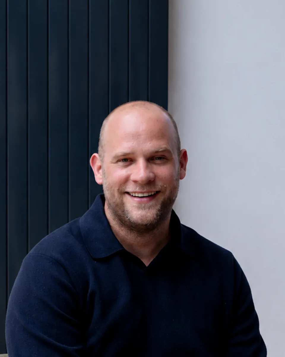 Joost de Kok, smiling, in a navy polo, in front of a light grey wall.