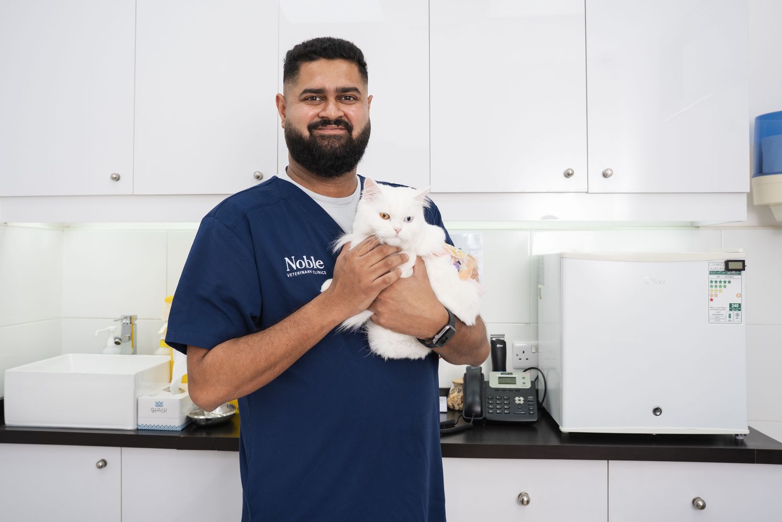 A veterinarian in navy scrubs holidng a white Persian cat.