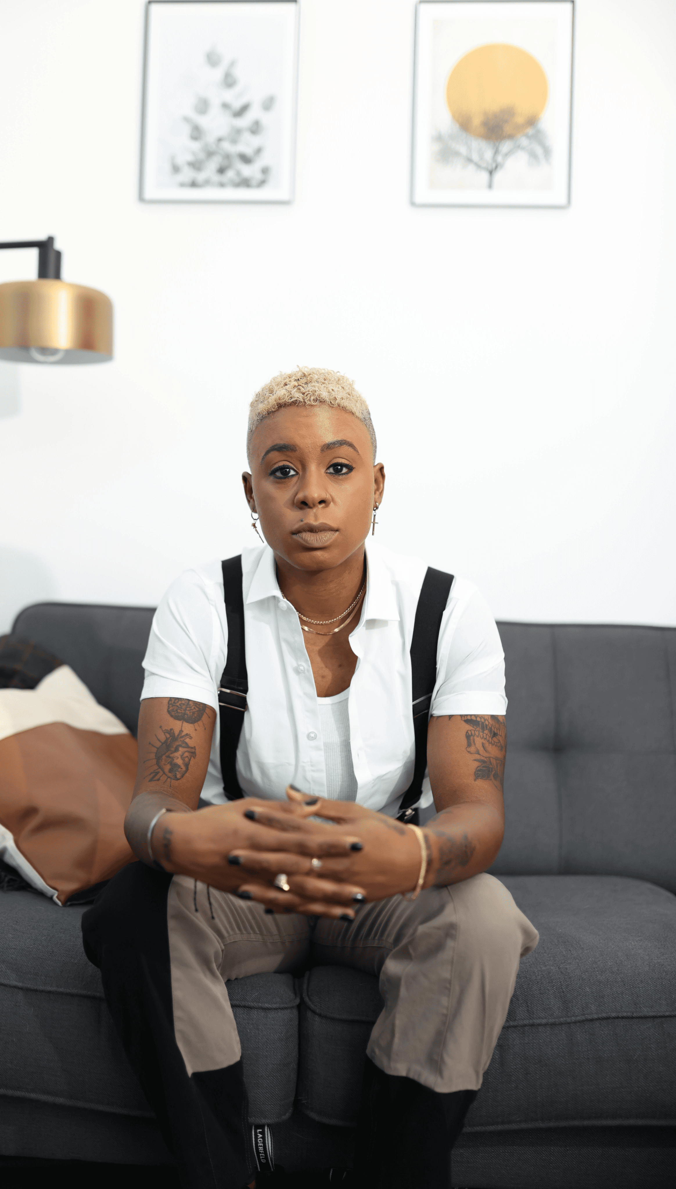 Ashleigh Warren sits on a couch, looking thoughtfully at the camera, with artwork on the wall behind her.
