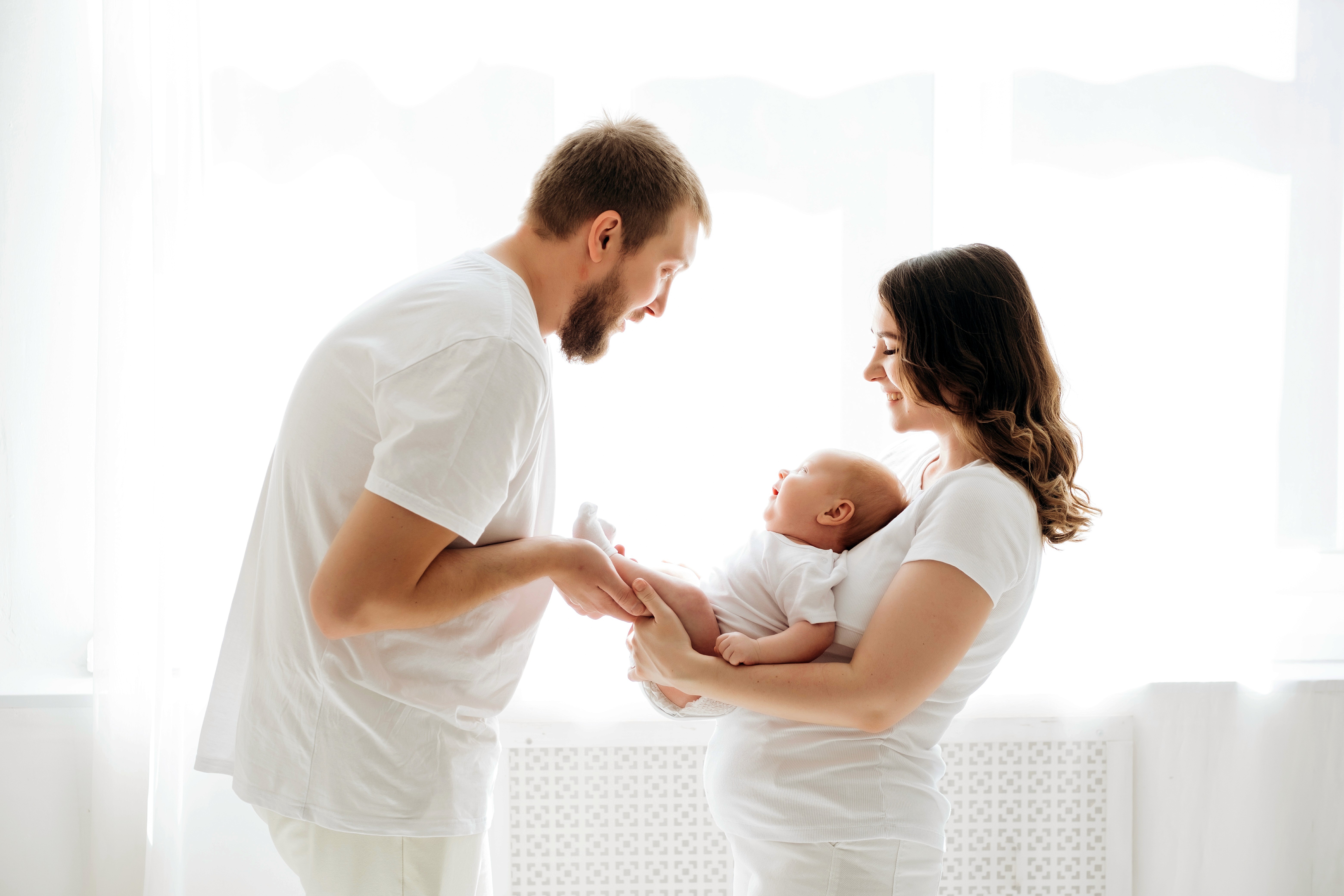 Parents holding their healthy newborn in soft natural light — the ultimate goal of neonatal research and care.