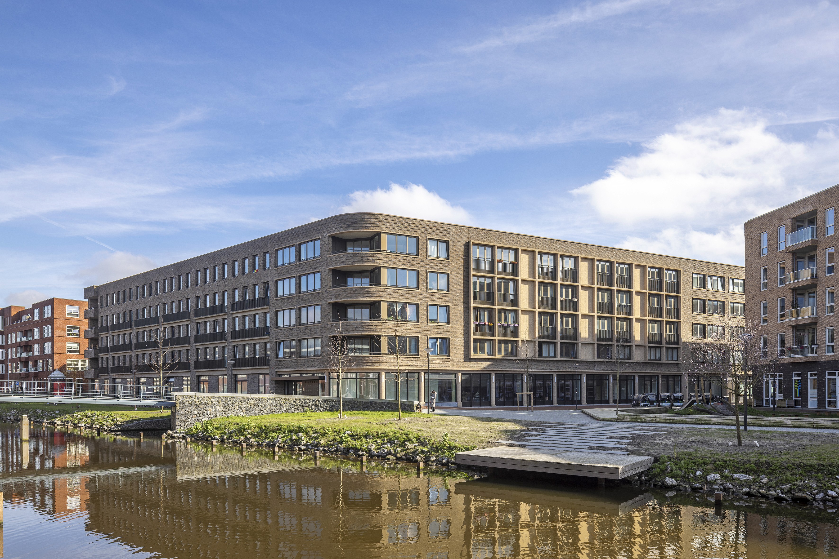 Een modern bakstenen gebouw aan het water met een blauwe lucht en wolken.