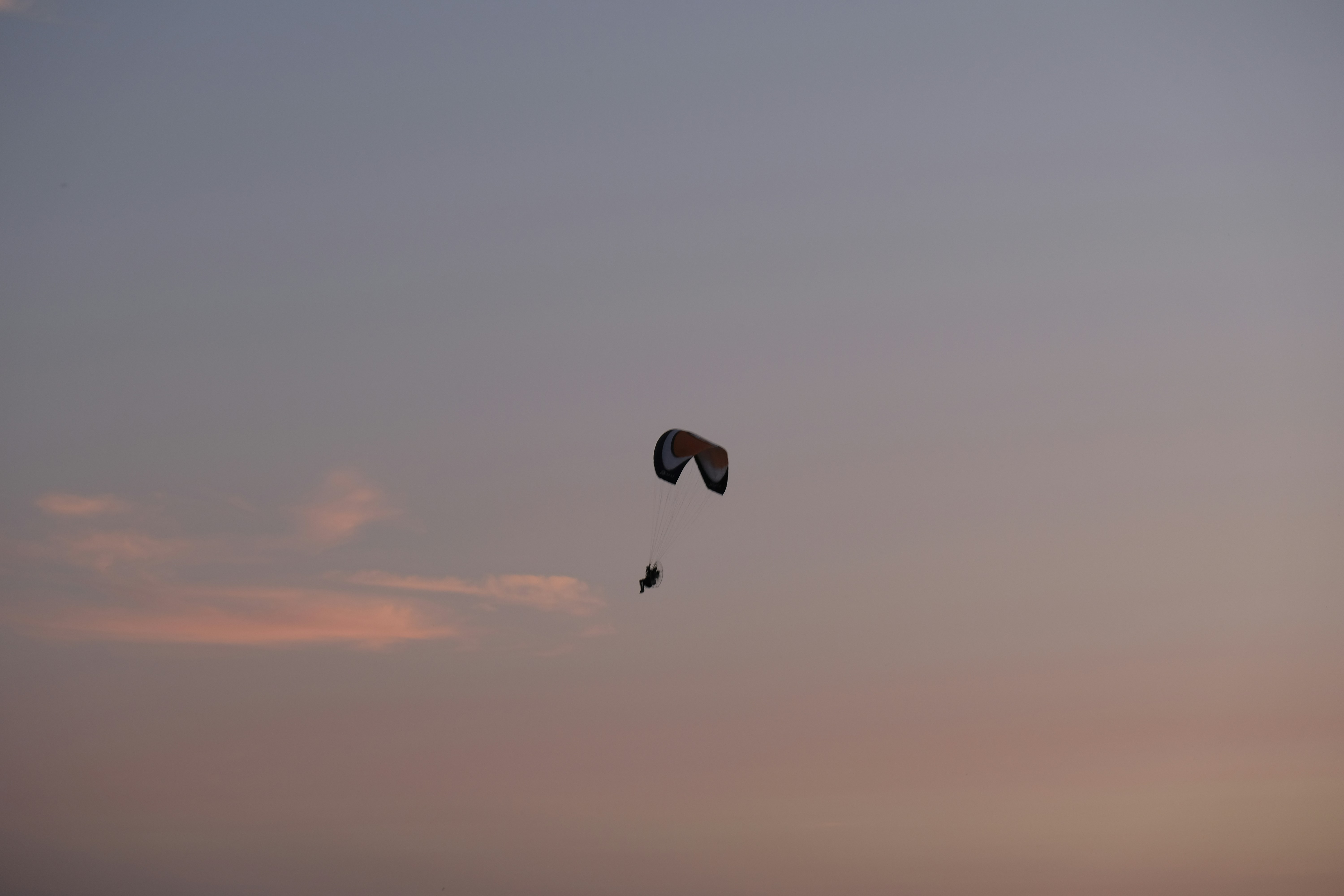 silhouette of person with parachute in mid air during sunset