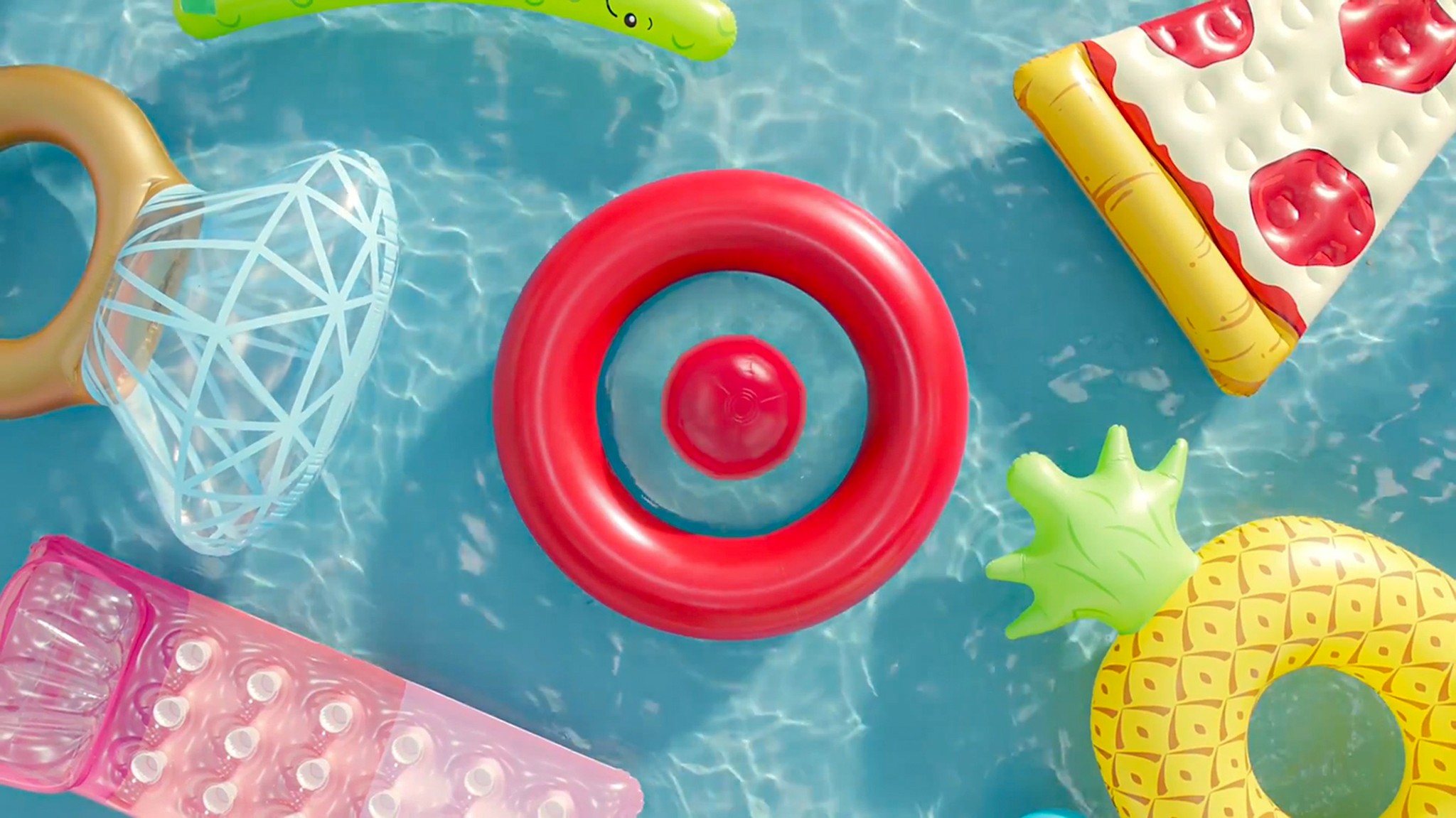 Red inflatable ring floating in a swimming pool, viewed from above, with colorful pool toys partially visible around it.