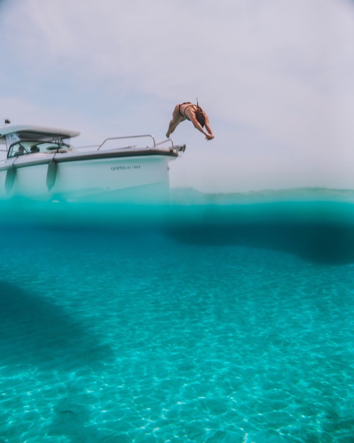 Person diving from white Axopar 37 yacht into crystal clear turquoise waters of the Cyclades.