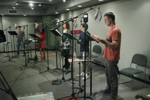 The Rebels voice cast in a single recording booth standing in front of microphones and music stands