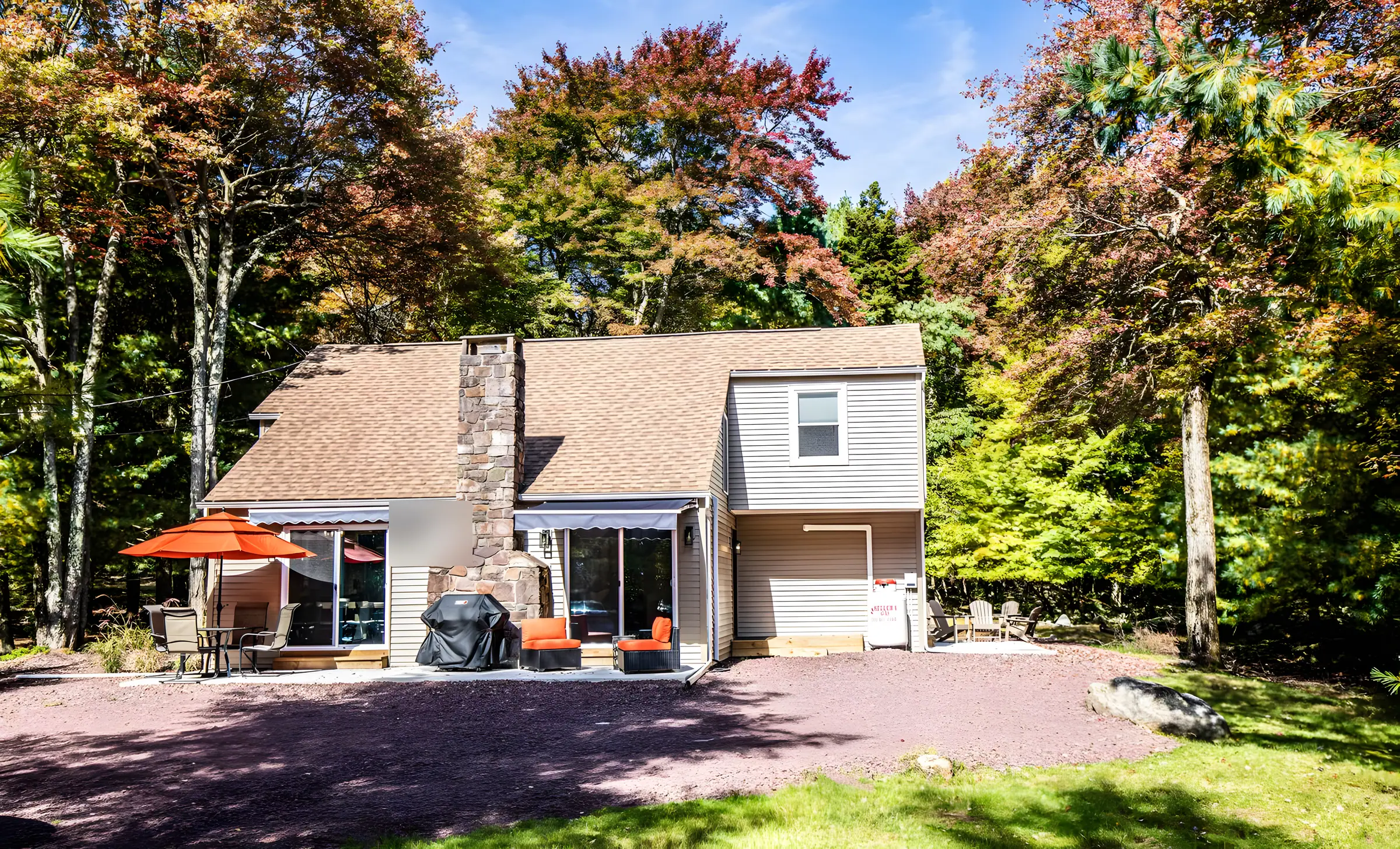 Tan two-story home with stone chimney, orange umbrella and fall trees at Divine on Lupine, Lake Harmony, PA