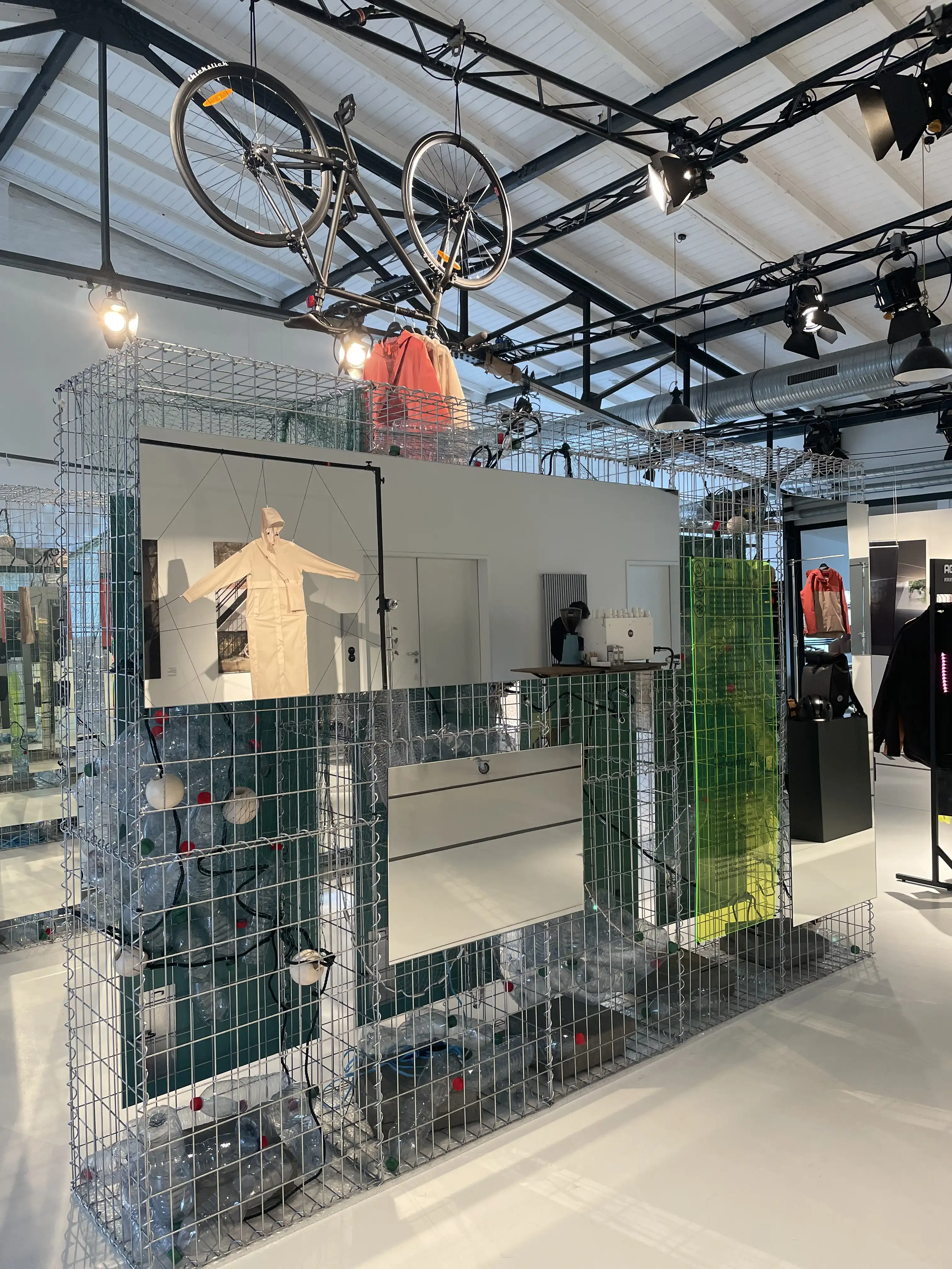 Wire-gabion display unit with monitor and bicycles mounted overhead at the AGU brand experience space.