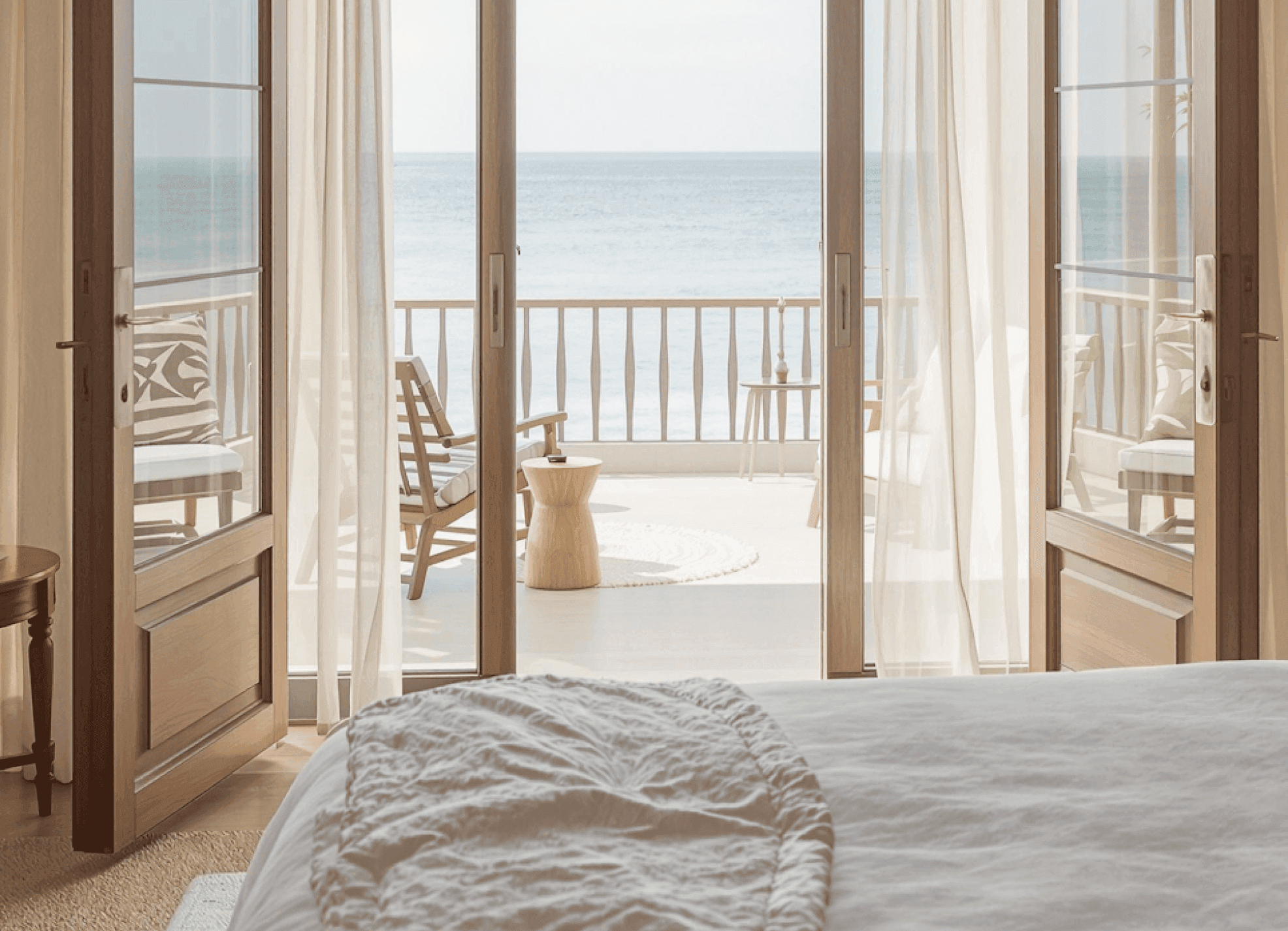 Serene oceanfront bedroom with flowing curtains and a cozy balcony seating area.