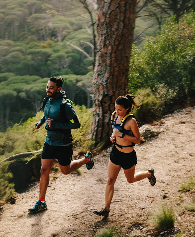 A man and woman trail running together through a misty forest on a dirt path