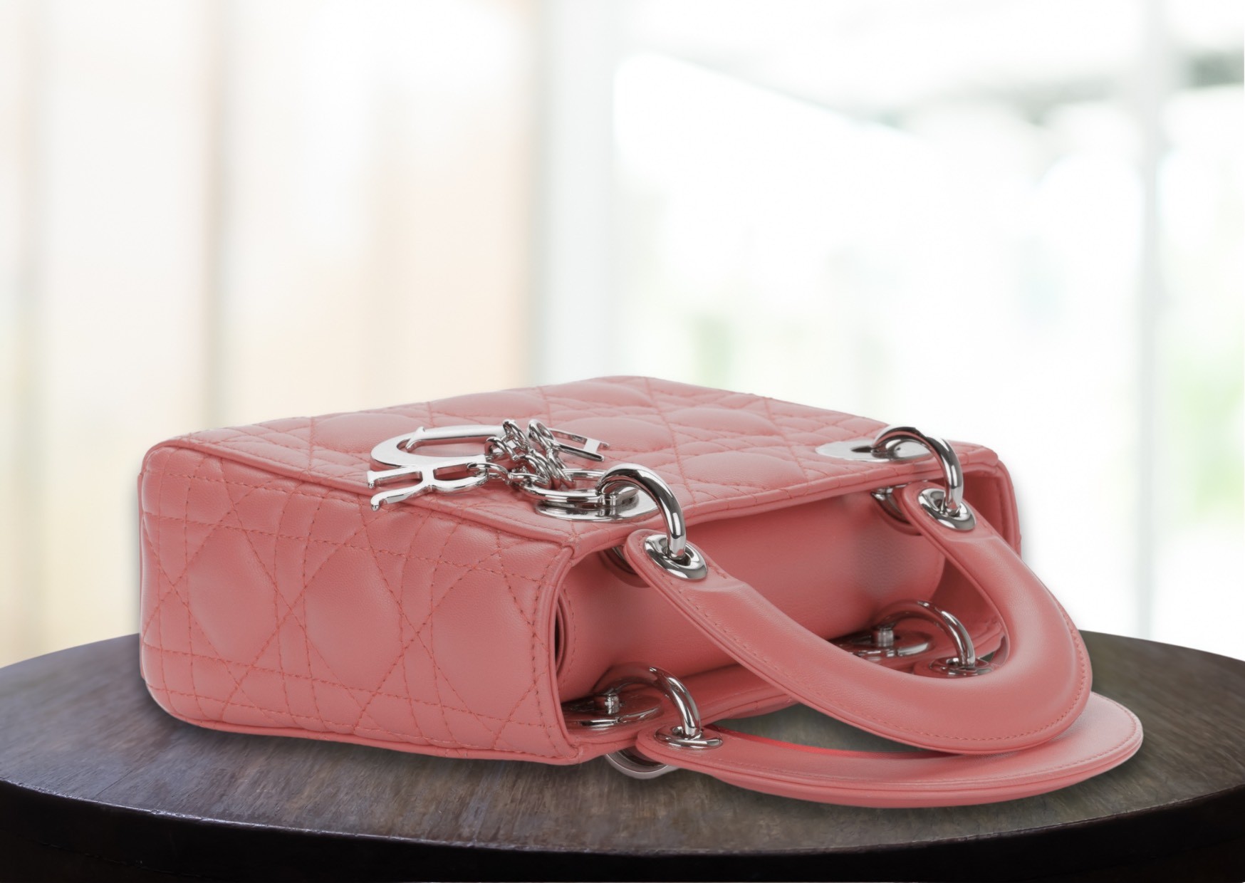 Chic pink Lady Dior purse, exuding luxury, laying on a pristine table with outdoor sun light - emulating sophistication.