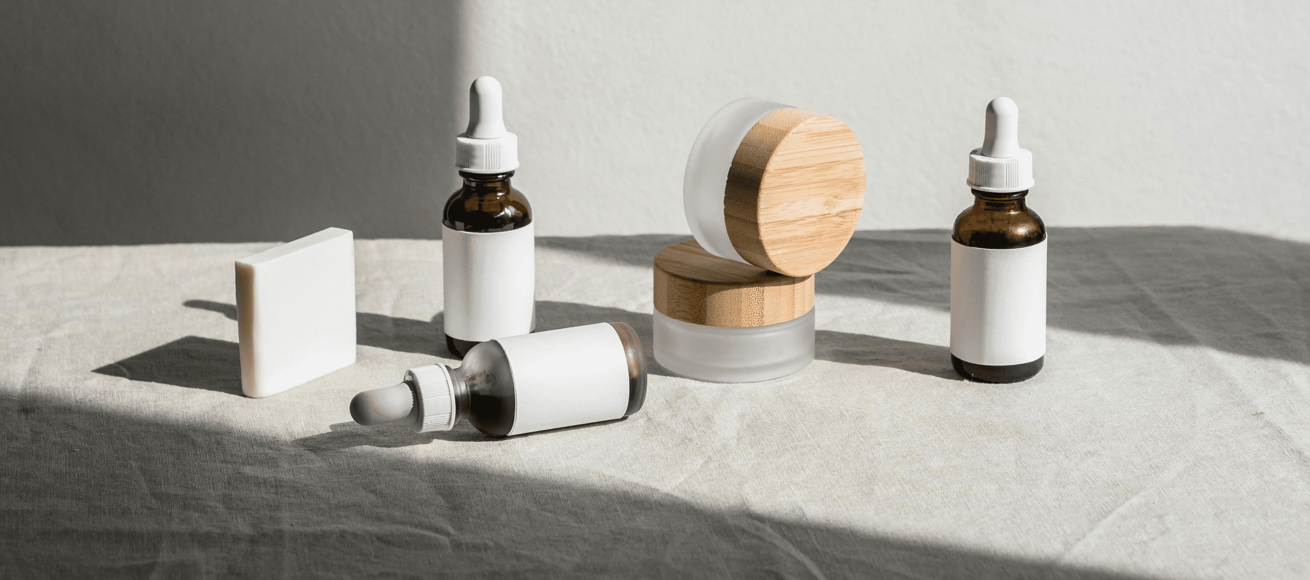Spa products: skincare serum bottles, cream jars, and soap bar on white cloth. Natural beauty products, self-care concept.
