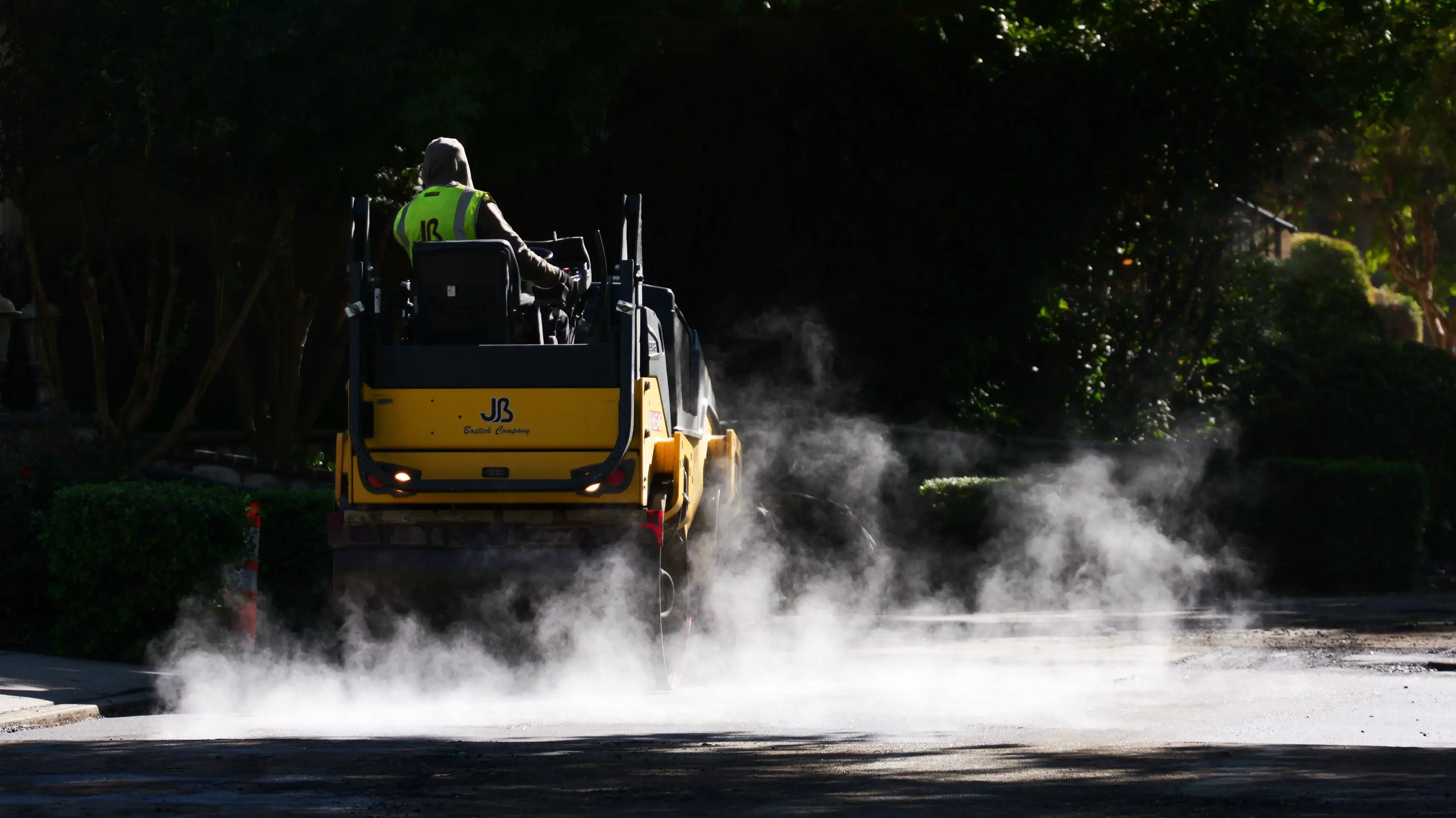 Asphalt roller compacting new pavement with steam rising