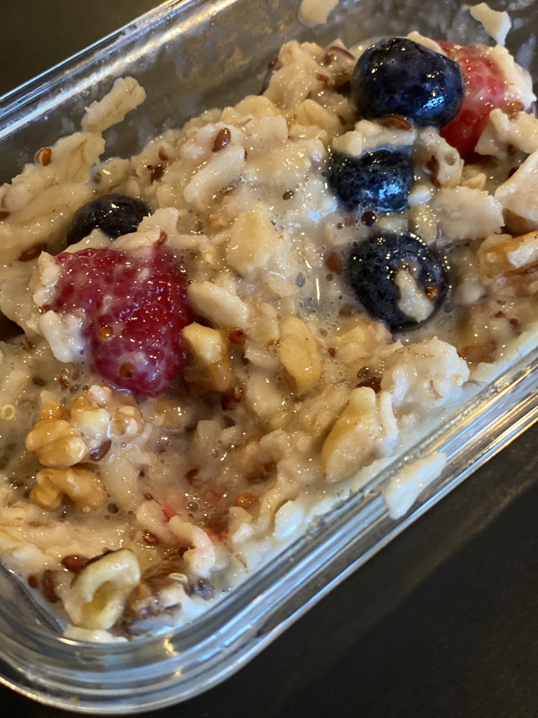 A clear container filled with oatmeal topped with fresh blueberries, raspberries, and walnuts, showcasing a nutritious and colorful breakfast option.