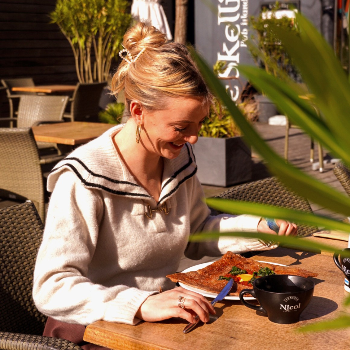 Photo du shooting. On y voit un femme blonde en train de manger une galette complète en extérieur.