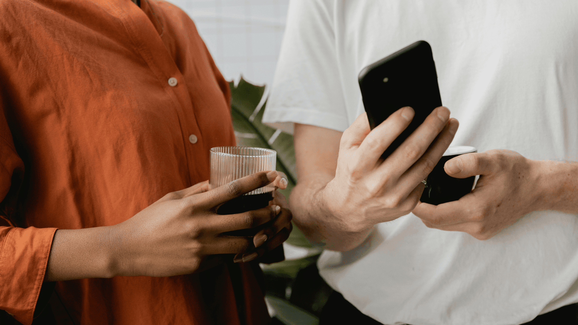 En som holder en kopp og en annen en mobiltelefon