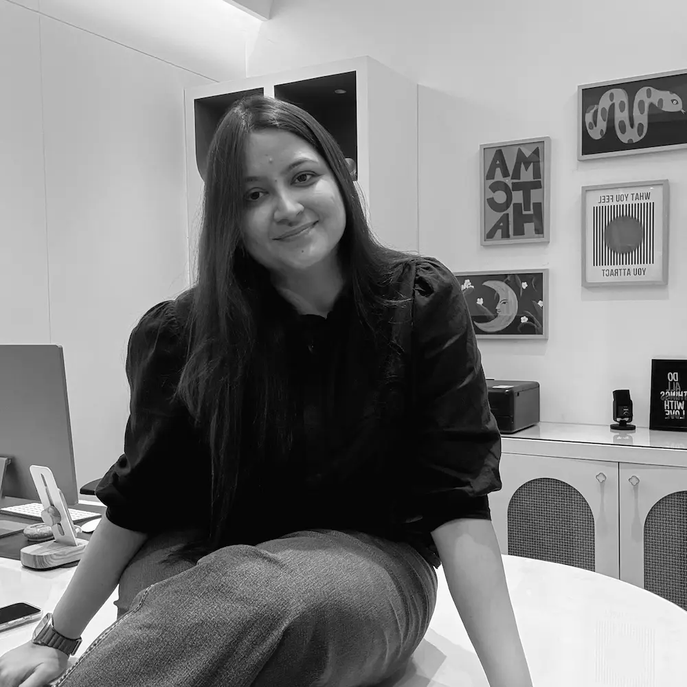 A person sits casually on a desk in a modern, monochrome office, featuring sleek technology, abstract wall art, and a minimalist decor theme.