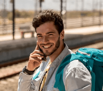 Homem com mochila em estação de trem falando ao telefone durante viagem