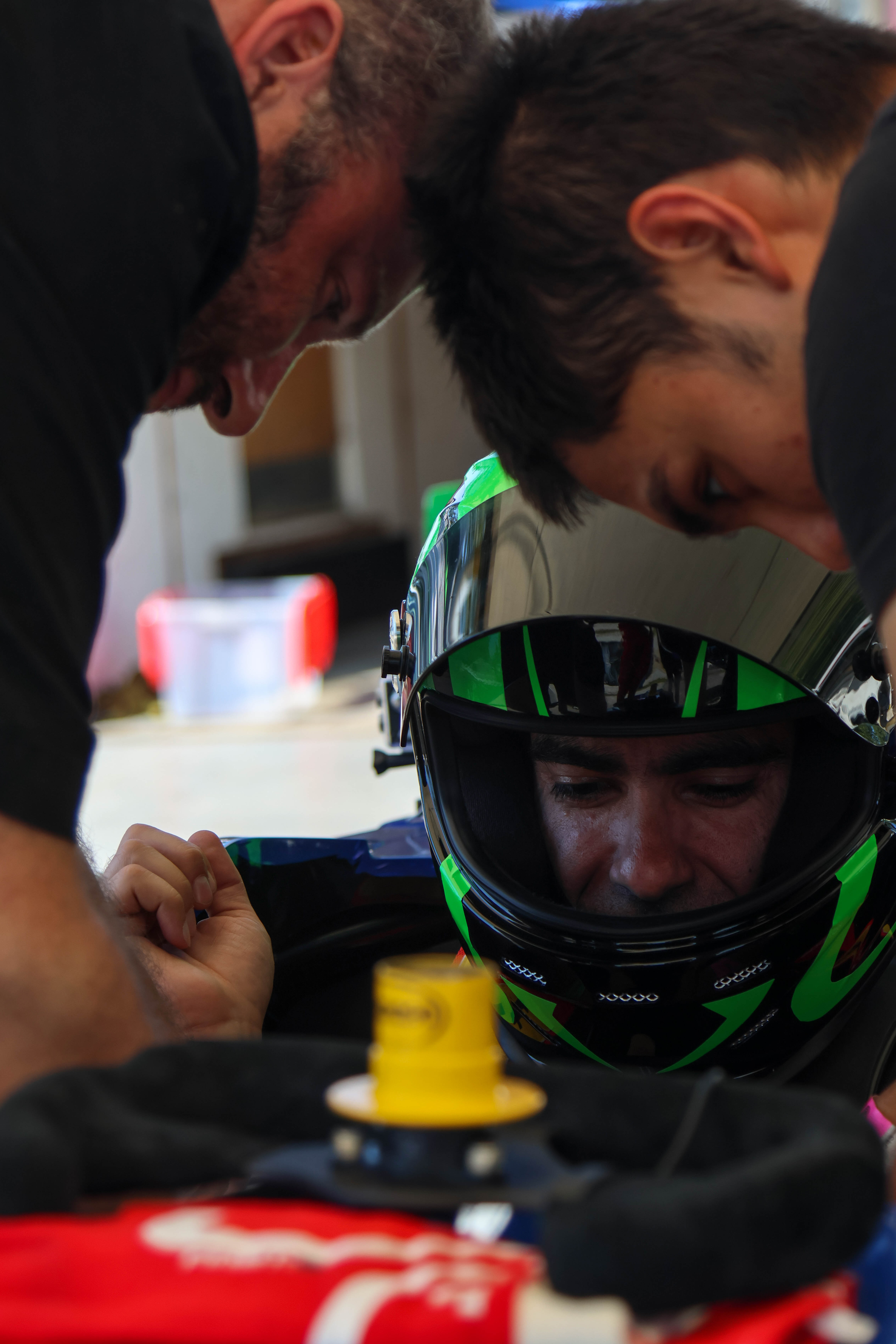 Two camera operators in a dimly lit studio adjust a large video camera. They wear headsets and caps, focusing intently. Mood is professional and focused.
