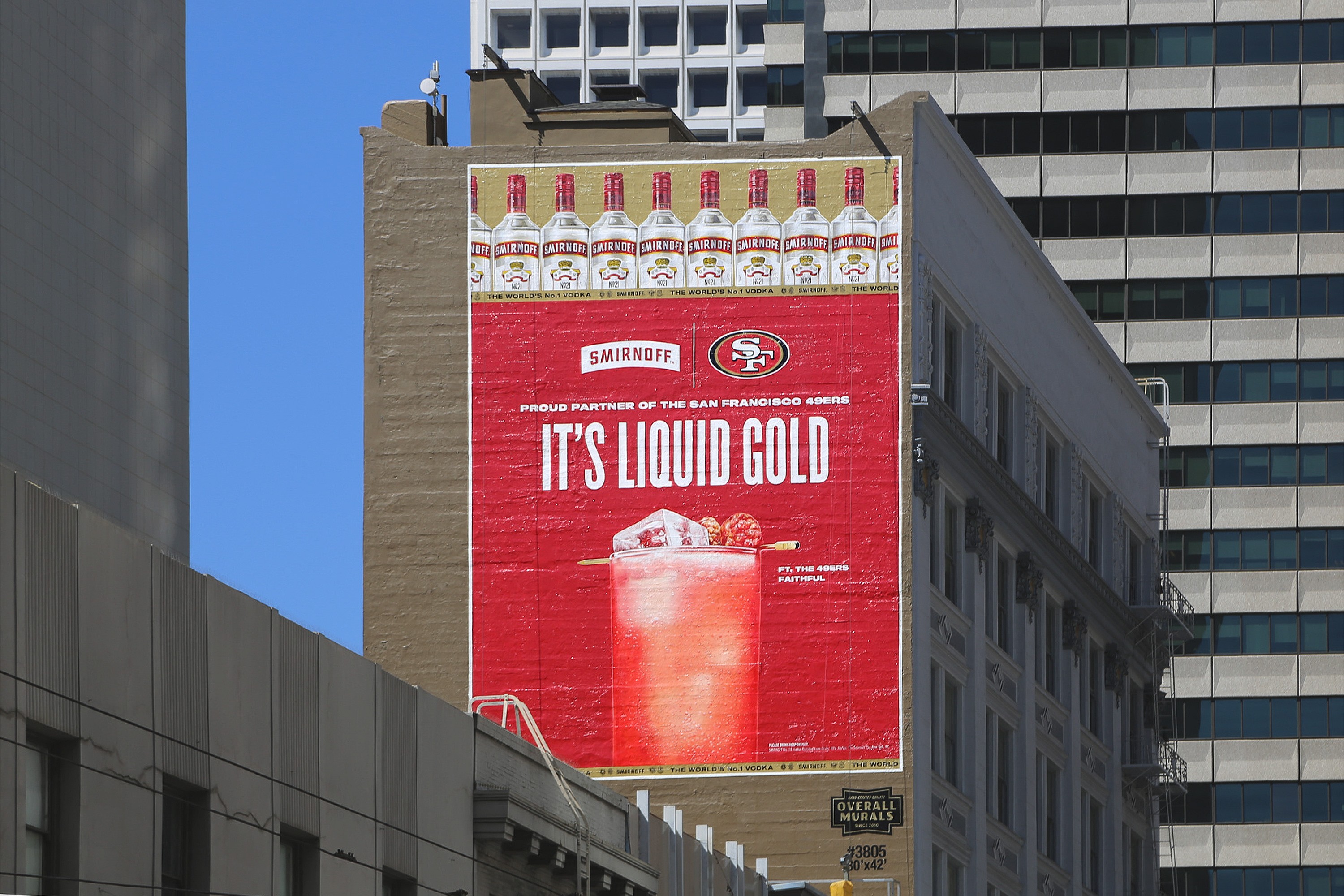 Advertisement on a building side for Smirnoff vodka, stating 'It's Liquid Gold' with a bucket of ice and vodka, and the San Francisco 49ers logo, highlighting their partnership.