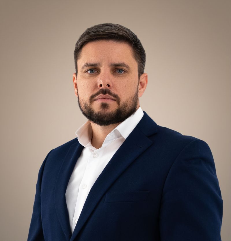 A confident person with short, styled hair and a leather jacket poses against a dark backdrop.
